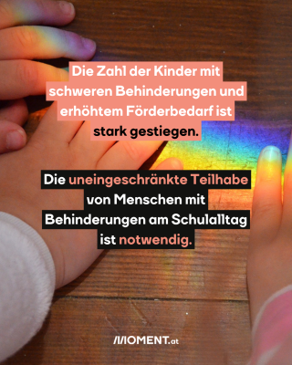 Kinderhände versuchen einen Regenbogen zu fassen, der wohl durch ein Glasgegenstand auf einen Holztisch geleuchtet wird. 